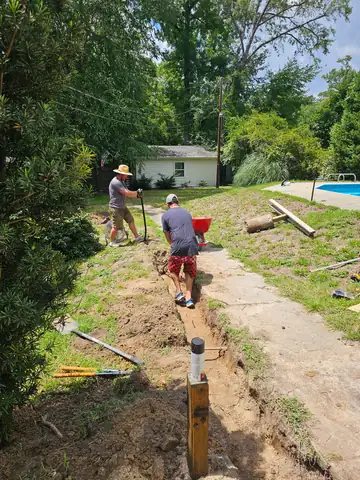 Two workers digging a drain trench along a concrete slab