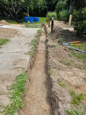 Drain trench dug along a sidewalk with drain pipe ready behind it
