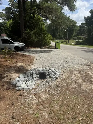 Culvert pipe under a gravel driveway entrance with rip-rap stone around the end