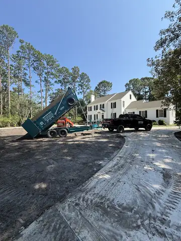 Dump trailer unloading base on a new driveway beside a white house