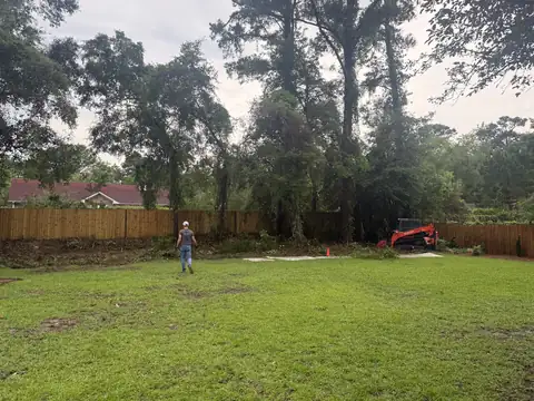 Backyard fence line cleared of overgrowth, Kubota track loader at the back