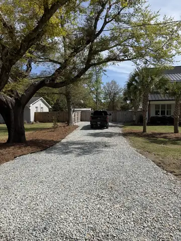 Finished gravel driveway under live oak trees leading to a home