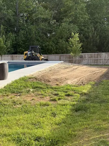 Strip of yard beside a pool graded smooth, compact track loader by the fence