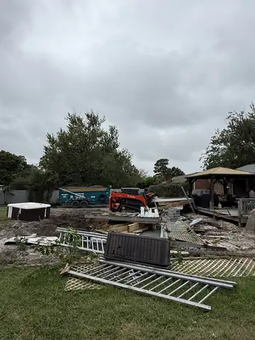 Backyard with a hot tub, fence panels and lattice torn out, Kubota track loader behind