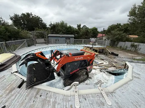 Kubota track loader with a grapple tearing out an above-ground pool from its deck