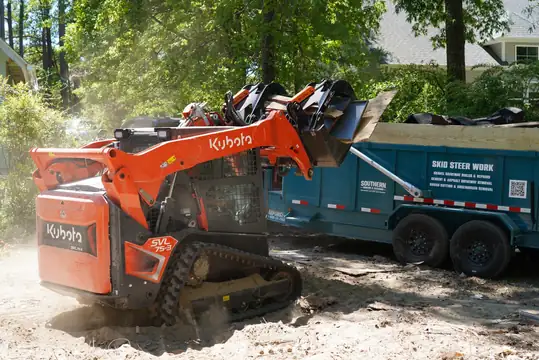 Kubota track loader with a grapple loading debris into the Southern Hauling dump trailer