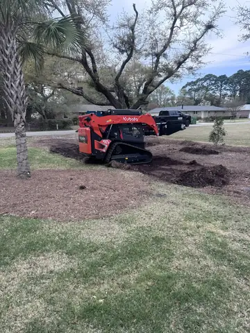 Kubota track loader clearing old landscape beds around a large oak tree