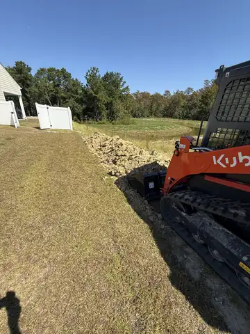 Kubota track loader digging along a side yard next to a white vinyl fence